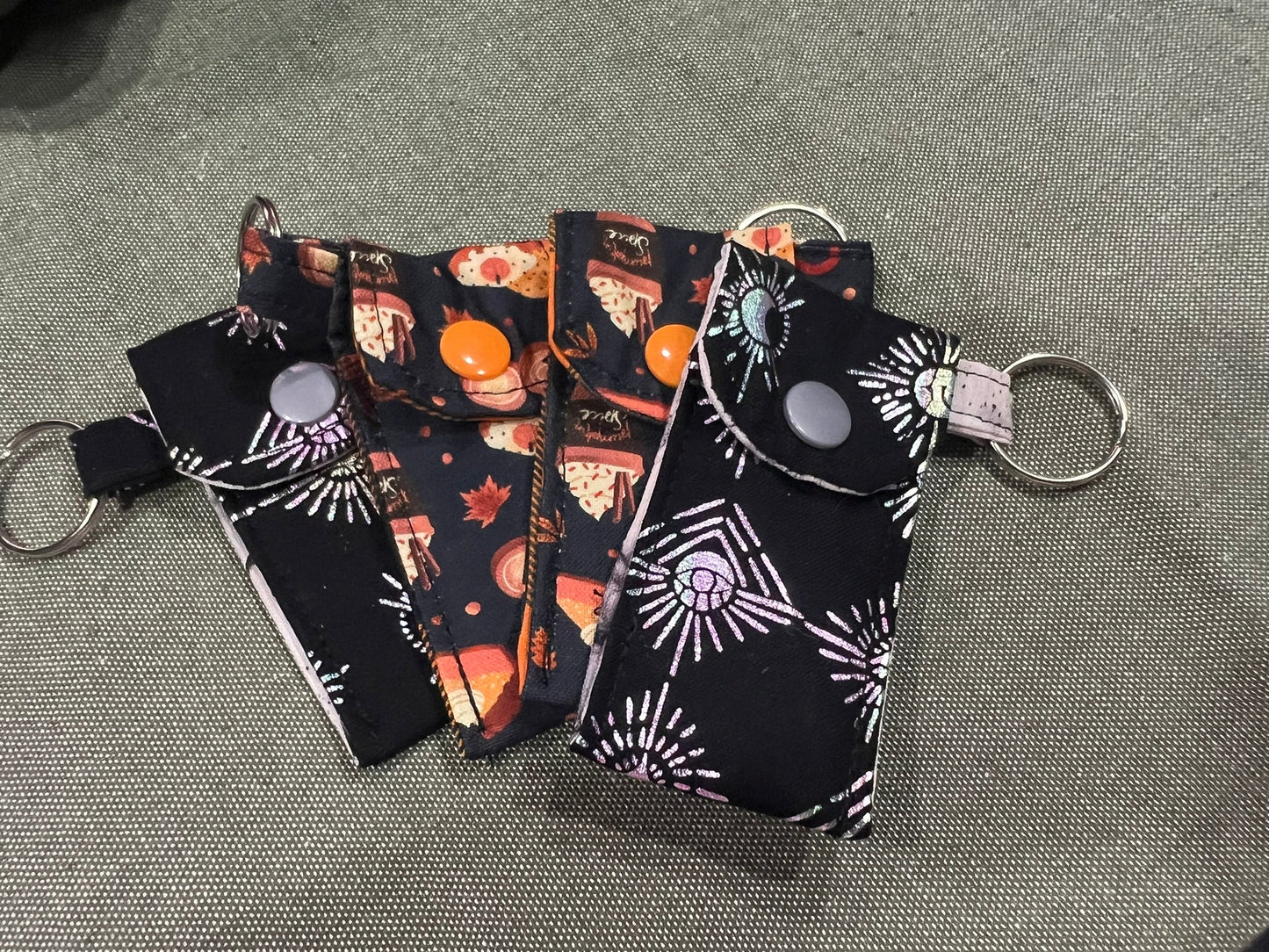 Set of four small fabric pouche keychains with fall-themed designs on a gray surface