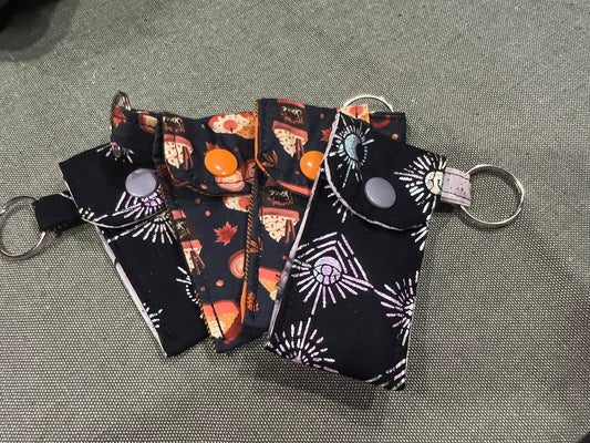 Set of four small fabric pouche keychains with fall-themed designs on a gray surface