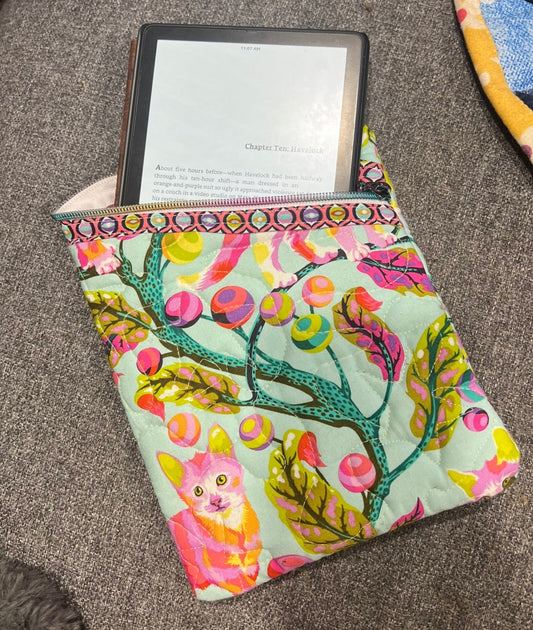 Colorful fabric case with a cat design holding an e-reader on a textured surface.